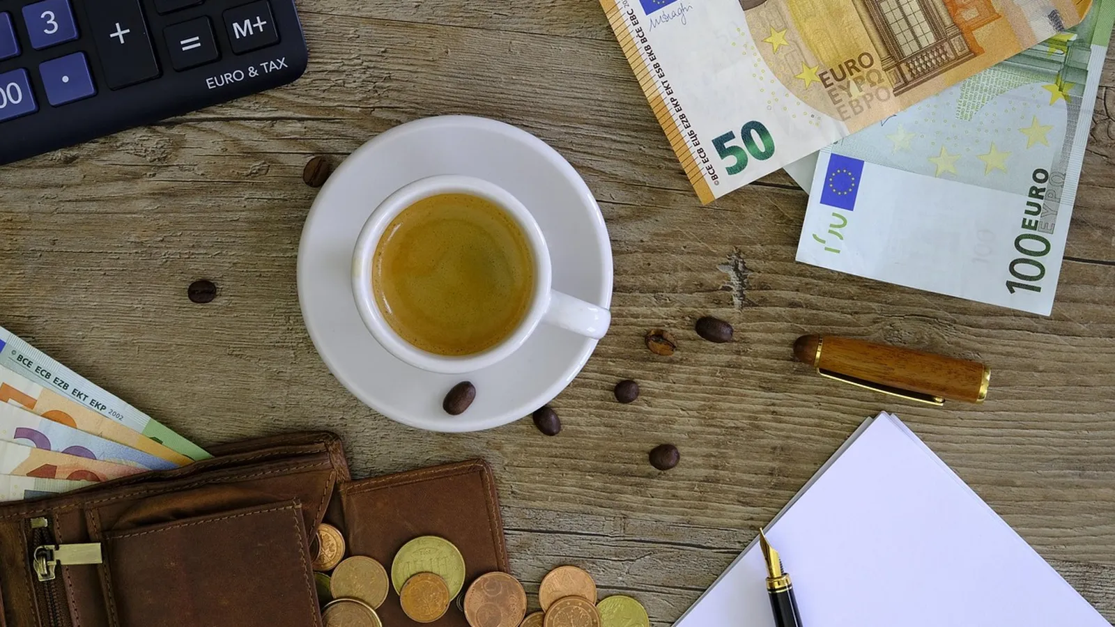 Taschenrechner, Euro-Scheine, Münzen und eine Geldbörse auf einem Holztisch